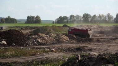 Kırmızı çöp kamyonu inşaat alanına toprak boşaltarak toz bulutu yaratıyor. Kırp