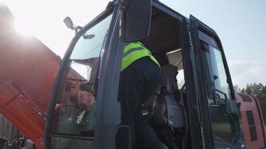İnşaat işçisi bir kazıcının kabinine tırmanıyor ve onu çalıştırmaya başlıyor. Kırp
