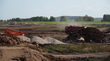 İnşaat makineleri büyük bir inşaat sahasında çakıl ve toprak taşıyor. Kırp