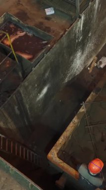 Endüstriyel işçiler fabrika ortamında büyük bir konteynıra dökülen karışımı denetliyor.