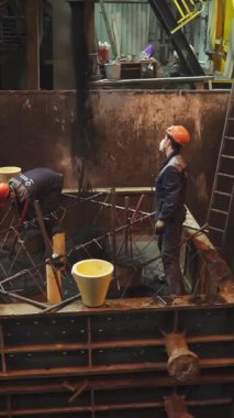 Dökümhane işçileri yoğun endüstriyel ortamda büyük bir küfe erimiş metal döküyorlar.