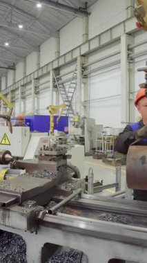 Torna makinesi işleten yetenekli bir metal işçisi modern bir endüstriyel fabrikada hassas parçalar üretiyor.