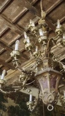 Süslü avize ahşap bir tavandan sarkıyor duvar örme duvarları ve altın çerçeveli sanat eserleri olan bir odada