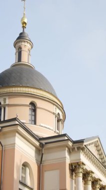 Mavi gökyüzünün altında çan kulesi ve kubbesi olan pembe ve gri bir kilise.