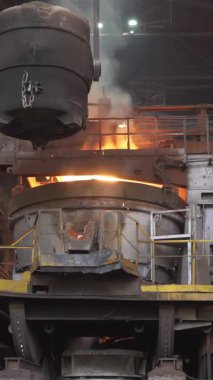 Asılı bir konteynırdan, çelik fabrikasındaki bir fırına sıvı metal dökülüyor.