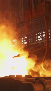 Çelik fabrikasındaki büyük bir konteynırdan dökülen erimiş metal kıvılcımlar ve duman yaratır.