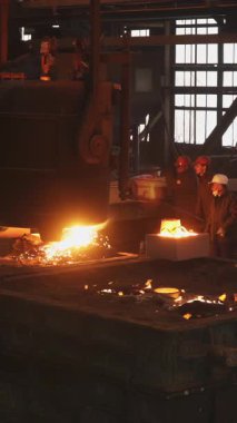 Dökümhane işçileri büyük bir endüstriyel kalıba erimiş metal döküyorlar.