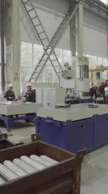 Fabrika işçileri modern bir endüstriyel tesiste büyük bir makinede metal parçaları birleştiriyorlar.