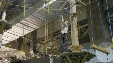 Güvenli kabloyu güvenli bir şekilde tırmanan dağcı, kapalı bir spor salonunda yüksek bir platforma tırmanarak odak ve hassasiyet gösteriyor. Yaratıcı