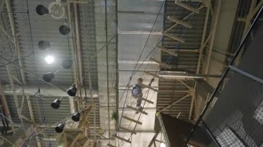 Tırmanışçılar, kapalı bir macera parkında zorlu ip köprüleri ve engelleri aşarak dikkatle manevra yapıyorlar. Yaratıcı