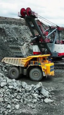 Büyük bir kazıcı açık bir maden ocağında bir çöp kamyonuna mayın yüklüyor.