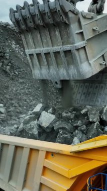 Açık bir maden ocağında büyük bir kazıcı cevheri çöp kamyonuna yüklüyor.
