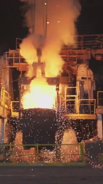 Çelik fabrikasındaki büyük bir konteynırdan dökülen erimiş metal kıvılcımlar ve duman yaratır.