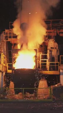 Çelik fabrikasındaki büyük bir konteynırdan dökülen erimiş metal kıvılcımlar ve duman yaratır.