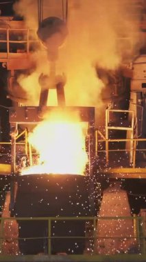 Çelik fabrikasındaki büyük bir konteynıra erimiş metal döküp kıvılcım ve duman çıkaran endüstriyel bir süreç.