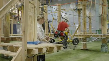 Belgrad, Sırbistan - Haziran 2025: Küçük çocuk kapalı sahada eğitmen nezaretinde zip hattına biniyor. Yaratıcı