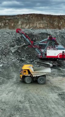 Büyük kazıcı madencilik alanında taşları çöp kamyonuna yüklüyor.