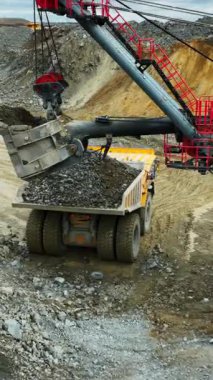 Büyük bir kazıcı açık bir madencilik operasyonunda taşları bir çöp kamyonuna yüklüyor.