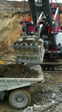 Büyük kazıcı madencilik alanında kaya ve mineralleri çöp kamyonuna yüklüyor.
