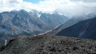 Yürüyüşçüler bir dağ sırtından geçerek, karlı tepelerin arasında yuva yapmış bir vadiyi nefes kesici bir şekilde görüyorlar. Medya