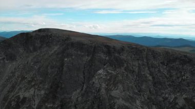 İHA görüntüsü yana doğru uçuyor ve berrak mavi gökyüzü ile görkemli kayalık bir dağ manzarasını ortaya çıkarıyor. Medya