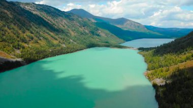 Yeşil orman dağlarıyla çevrili güzel bir buzul gölü üzerinde uçan çarpıcı bir hava perspektifi. Medya