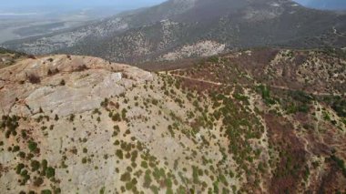 Hava görüntüleri engin, kayalık ve tepelik bir arazide seyrek yeşil bitki örtüsüyle uçuyor. Medya