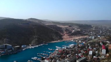 Yeşil tepelerin arasına yerleştirilmiş yatlarla dolu bir marinası olan pitoresk bir sahil kasabasının havadan görünüşü. Medya