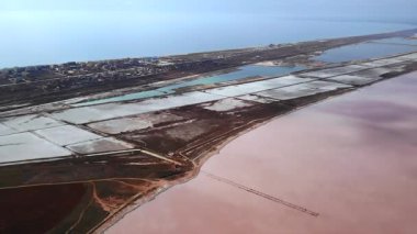 Güneşli bir günde mavi denizin yanında güzel pembe bir tuz gölünün üzerinde uçan hava manzarası. Medya