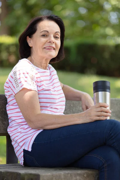 ベンチに座って公園でコーヒーを飲んでいる老女は — ストック写真