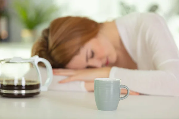 熟睡的年轻女子倒在咖啡壶旁边的桌子上 — 图库照片