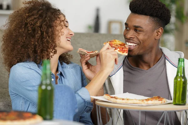 smiling young couple with pizza on sofa at home
