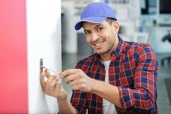 幸せな電気技師は壁の取付け具の電気線を引き締める — ストック写真