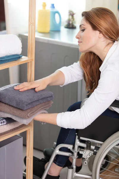 坐在轮椅上的年轻残疾妇女把干净的衣服收起来 — 图库照片