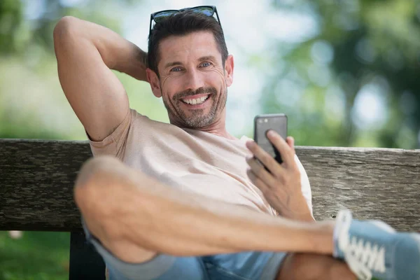 坐在户外长椅上快乐英俊的男人 — 图库照片