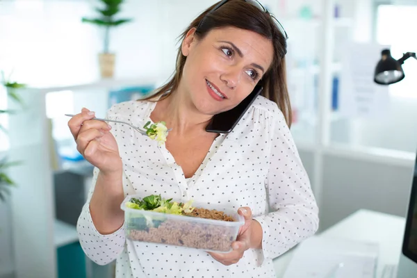 woman eating salad and taking call on smartphone