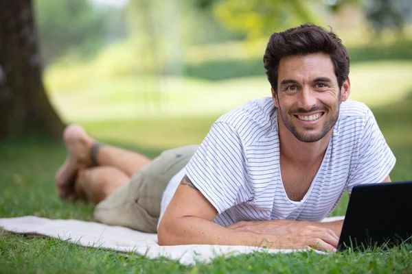 年轻人在公园里用笔记本电脑躺在草地上 — 图库照片