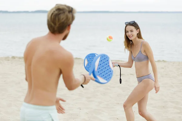 身穿泳衣的夫妻在海滩上玩球拍和球 — 图库照片