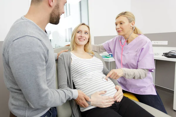 妊娠中の若い夫婦と相談する女性医師は — ストック写真