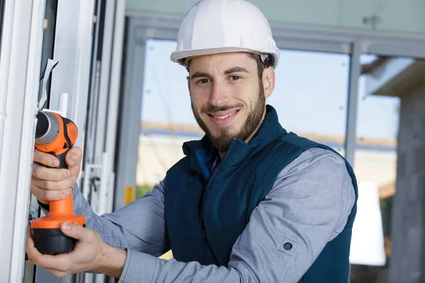 smiling contractor using cordless power-tool on window frame