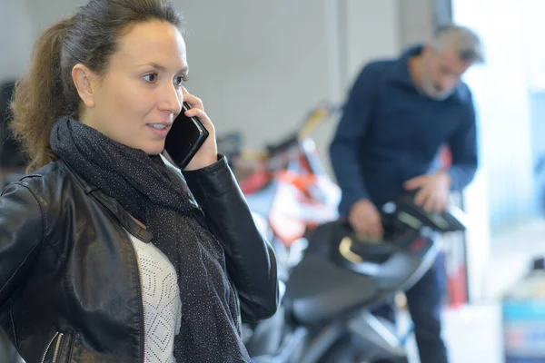バイク屋に立っている間にスマートフォンを使う女性は — ストック写真