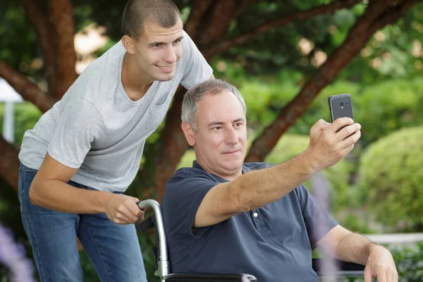 Hombre Silla Ruedas Tomando Selfie Con Hombre Joven Empujando Silla — Foto de Stock