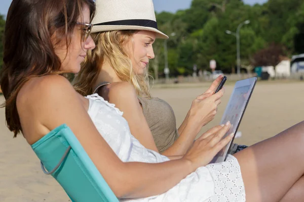 Mulheres Usando Gadget Enquanto Banhos Sol Praia — Fotografia de Stock