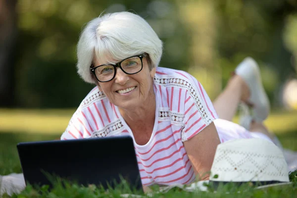 躺在公园时 用笔记本电脑微笑的老妇人 — 图库照片