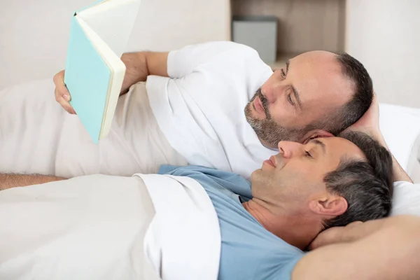 快乐的同性恋夫妇看书躺在床上 — 图库照片
