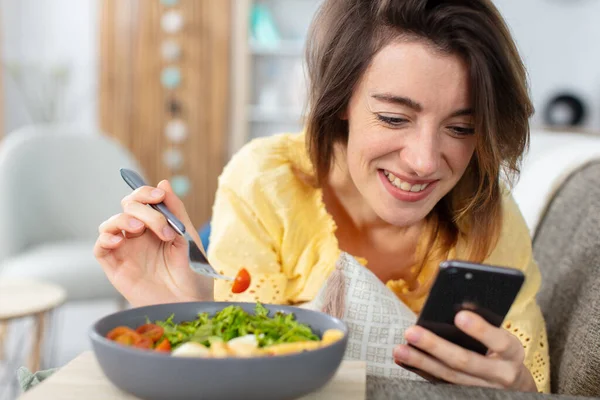 若い女性がスマホを見てサラダを食べる — ストック写真