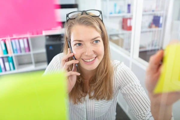 Młoda Bizneswoman Rozmawia Przez Telefon Odklejając Przypomnienie — Zdjęcie stockowe