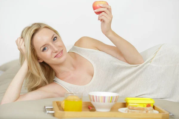 素敵な若い女性がベッドでリンゴを食べる — ストック写真