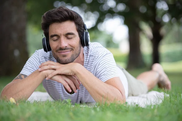 Człowiek Zamkniętymi Oczami Leżący Trawie Słuchający Muzyki — Zdjęcie stockowe