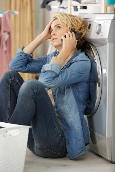 Rozrušený Hospodyňka Sedí Podlaze Prádelně Telefonu — Stock fotografie